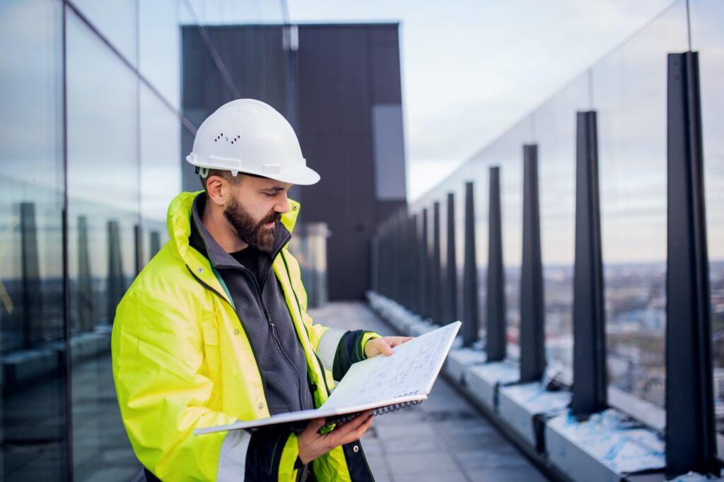 Man engineer standing on construction site, holding blueprints.